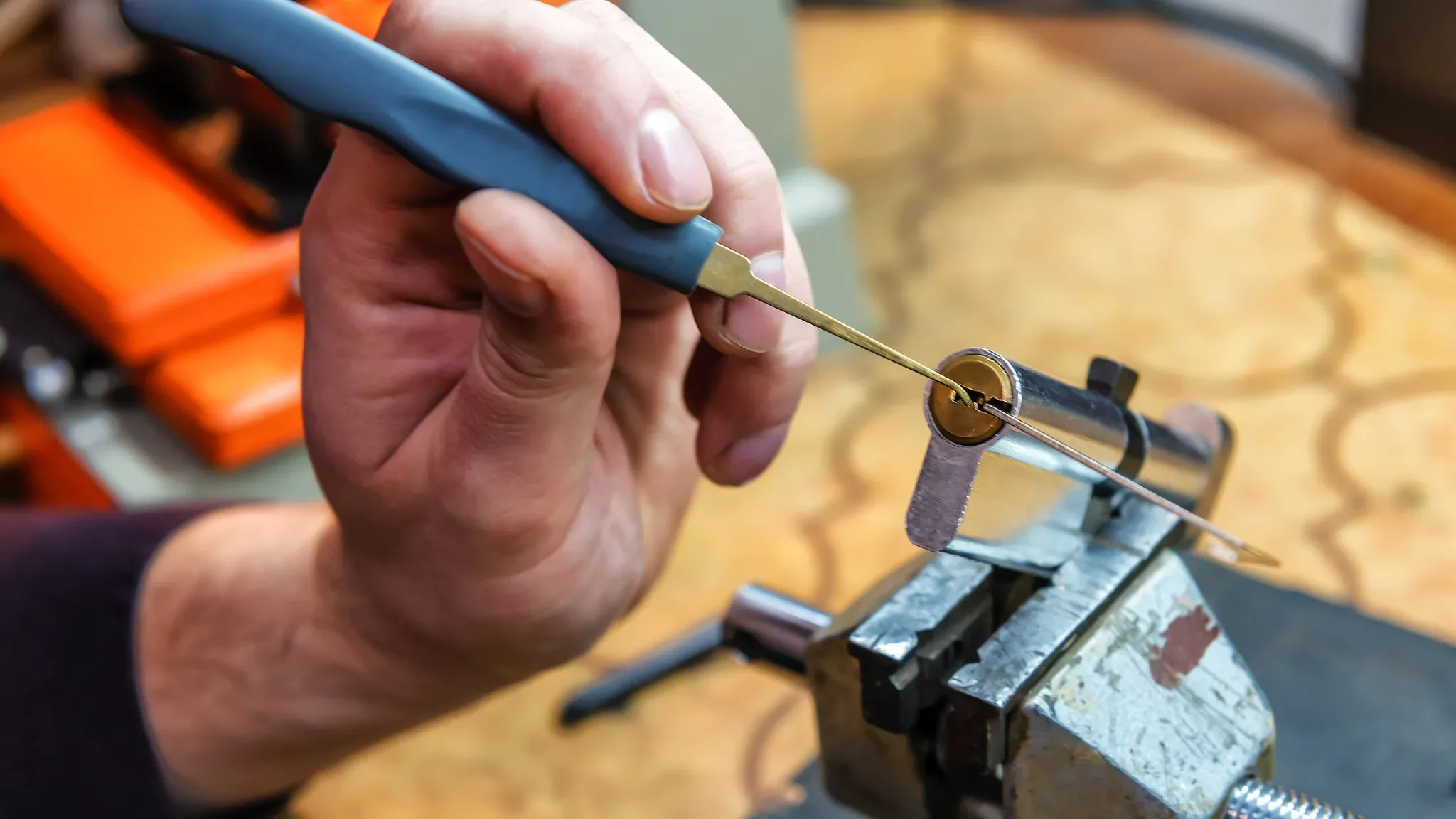 An extreme close-up shows a hand using a blue-handled needle file to shape the teeth of a brass-colored key blank clamped in