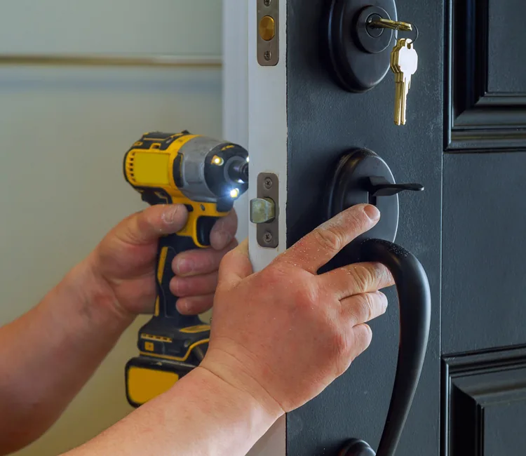 Locksmith using power drill to install deadbolt lock on dark door.